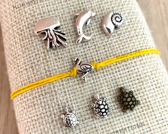 May include: A yellow string bracelet with silver charms of a jellyfish, dolphin, seashell, flamingo, and two turtles. One turtle charm is silver and the other is brown.