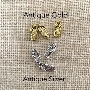 May include: Three antique gold-colored metal beads and three antique silver-colored metal beads shaped like figures holding circular objects. The text Antique Gold is positioned above the gold beads, and Antique Silver is below the silver beads.