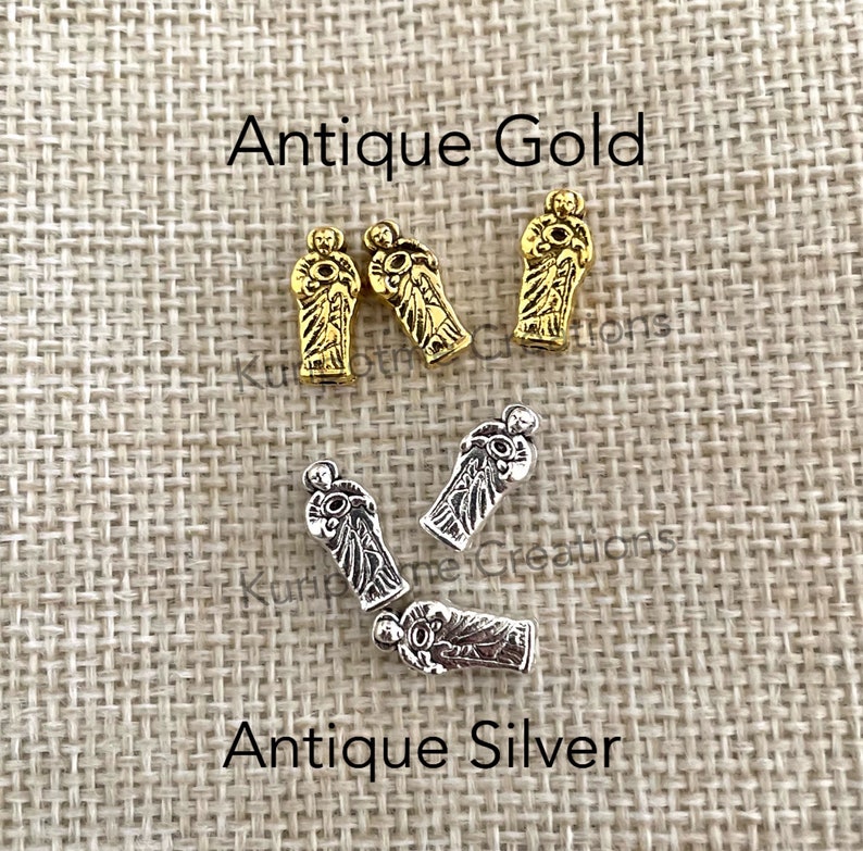 May include: Three antique gold-colored metal beads and three antique silver-colored metal beads shaped like figures holding circular objects. The text Antique Gold is positioned above the gold beads, and Antique Silver is below the silver beads.