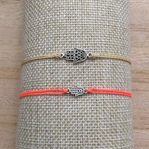 May include: Two bracelets with hamsa hand charms. The top bracelet is beige and the bottom bracelet is orange.