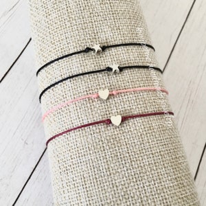 May include: Four friendship bracelets with different colored cords and silver charms. Two bracelets have star charms and two have heart charms.