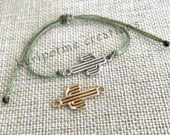 May include: A green string bracelet with a silver cactus charm. A gold cactus charm is also shown separately.