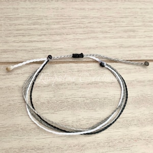 May include: A white, gray, and black braided friendship bracelet with black bead accents.