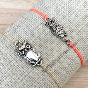 May include: Two friendship bracelets with silver owl charms. One bracelet is made with coral colored cord and the other with a natural colored cord.