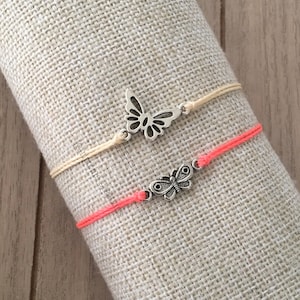 May include: Two bracelets with butterfly charms. One bracelet is coral pink and the other is beige.