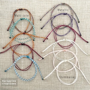 May include: A set of nine colorful friendship bracelets with different patterns and colors, including multi-color, metallic, and shimmering. The bracelets are made of thin cords and are tied with knots.