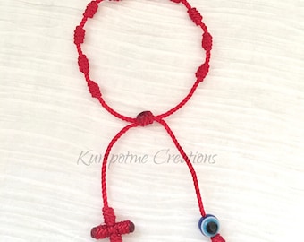 May include: Red string bracelet with a knotted design, a small red cross charm, and a blue evil eye charm.