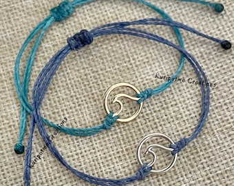 May include: Two adjustable bracelets with wave charms. One bracelet is teal, the other is blue. The wave charms are gold and silver. The text "Kuripotme Creations" is visible on the image.