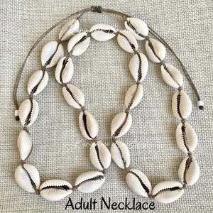 May include: A necklace made of natural cowrie shells strung on brown cord. The necklace is approximately 20 inches long and has a simple, elegant design.  Adult Necklace.