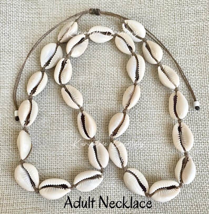 May include: A necklace made of natural cowrie shells strung on brown cord. The necklace is approximately 20 inches long and has a simple, elegant design.  Adult Necklace.