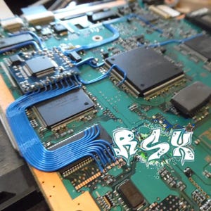 May include: Close-up of a green circuit board with blue wires and several black chips. The board has a white graphic with the text "BSU" on it.