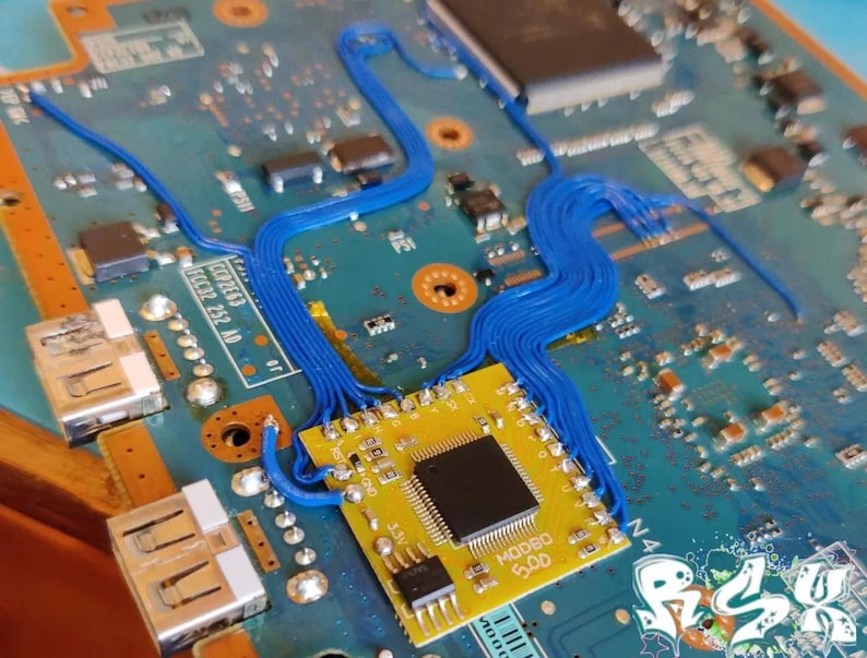 K&ouml;nnte beinhalten: Nahaufnahme einer blauen Leiterplatte mit einem gelben Chip mit der Aufschrift "MOORO 5.00". Blaue Dr&auml;hte sind &uuml;ber die Platine gef&uuml;hrt.