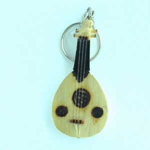 May include: A wooden keychain shaped like a oud, a traditional Middle Eastern stringed instrument. The keychain is light brown with black details and a silver key ring.