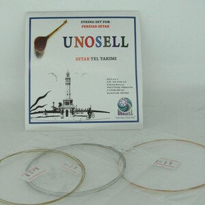 以下が含まれることがあります： ペルシャセタール用の弦セットで、パッケージには「UNOSELL」のブランド名が記載されています。 パッケージには弦楽器のイラストと海岸の風景が描かれています。 3つの弦セットが見えます。