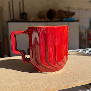 May include: A set of three ceramic mugs with a speckled, matte finish. The mugs are in shades of cream, light brown, and dark brown. Each mug has a simple, minimalist design and a rounded handle. The mugs are likely for coffee or tea.