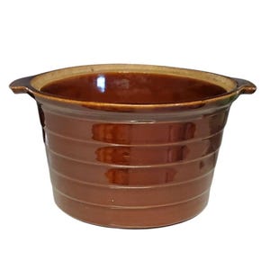 May include: A round, brown glazed ceramic bowl featuring a series of horizontal ridges along the exterior walls. The bowl has a wide, open top and two small, integrated handles extending from opposite sides of the rim, with a smooth, glossy finish.