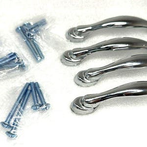 Può includere: Un set di quattro maniglie per mobili cromate lucide con viti abbinate. Le maniglie hanno un design curvo e sono presentate su una superficie bianca. Le viti sono in sacchetti di plastica trasparente.