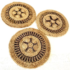 May include: Three round woven placemats. Each placemat has a natural tan colour with a dark brown star in the centre and a decorative border. The placemats are made of a natural fibre material.