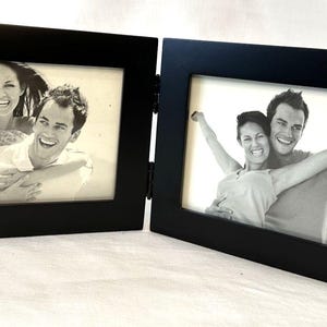 Puede incluir: Un marco de fotos doble negro con bisagras y dos aberturas de 10x15 cm. Cada marco contiene una fotografía en blanco y negro de una pareja sonriente. La marca "MALDEN" es visible en un marco.