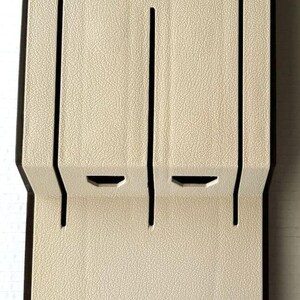 Op de afbeelding: Een beige, verticale organizer met een getextureerd oppervlak en donkerbruine rand. De organizer heeft sleuven en uitsparingen, met het woord "Cutco" bovenaan. Het is ontworpen om items vast te houden.