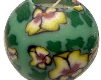 May include: A round green candle with a floral design. The candle has yellow and pink flowers with green leaves.