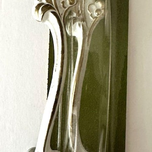 May include: White and gold decorative cabinet pulls with an ornate floral design. The pulls are packaged on a green backing card. The handles are approximately 15 cm long.