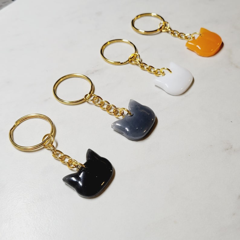 Pu&ograve; includere: Quattro portachiavi dorati con ciondoli a forma di gatto di diversi colori. I ciondoli sono nero, grigio, bianco e arancione.
