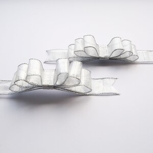May include: Two silver satin bows with a shimmery finish. The bows are tied with tails and are ready to be used for gift wrapping or decorating.