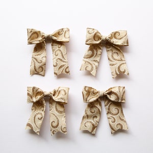 May include: Four beige bows with a gold swirl pattern. The bows are arranged in a square pattern on a white background.
