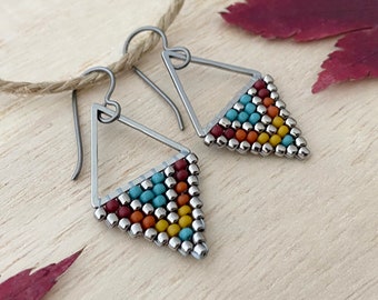 May include: A pair of silver triangle earrings with colorful beaded accents. The beads are in shades of red, orange, yellow, turquoise, and silver.