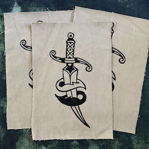 Könnte beinhalten: Drei beige Stoffpatches mit einer Schwarz-Weiß-Illustration eines Dolches mit einem dekorativen Griff. Der Dolch ist mit einem Band umwickelt und hat eine spitze Spitze.