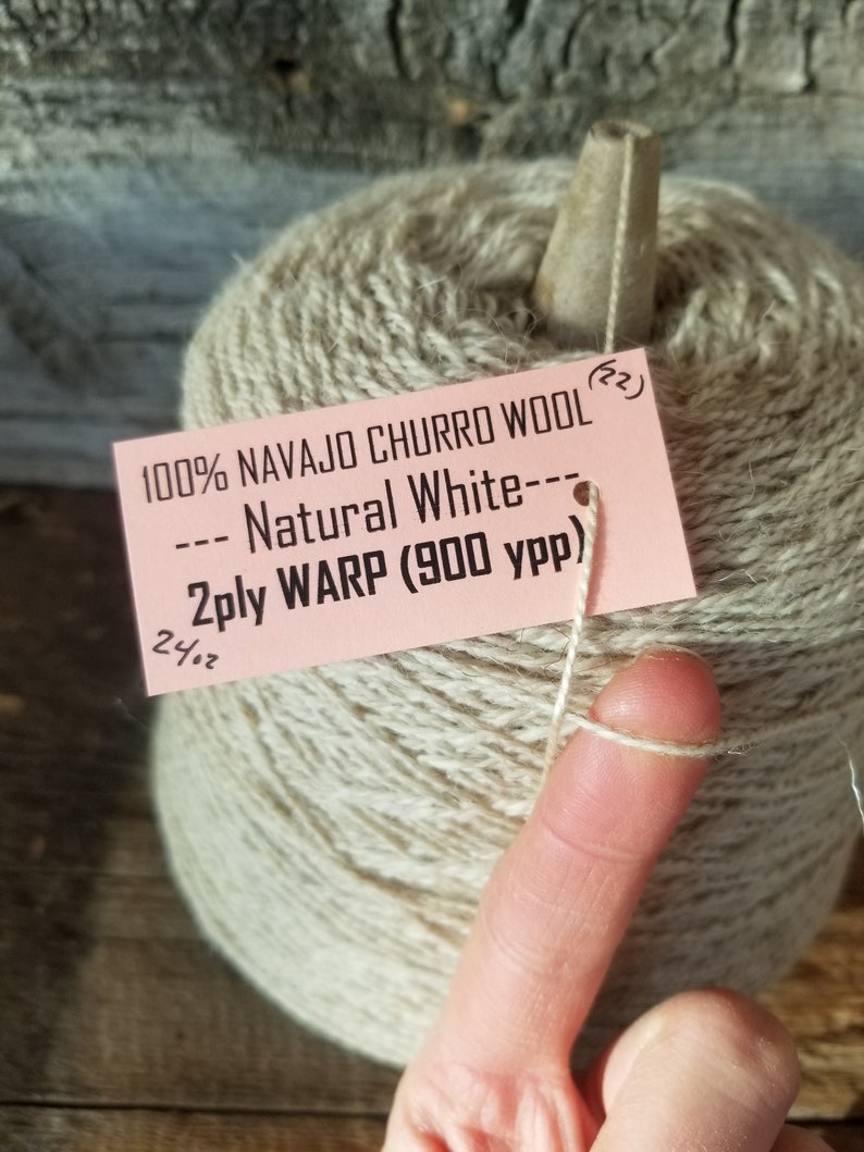 May include: A skein of 100% Navajo Churro wool yarn in natural white. The yarn is 2-ply warp and has 900 yards per pound. The skein is wrapped around a wooden dowel.