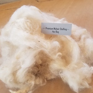 May include: A close-up of a large pile of white mohair stuffing. A white label reads "---Premium Mohair Stuffing--- 4oz Bag".