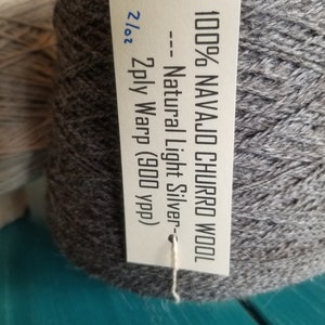 May include: A skein of 100% Navajo Churro wool yarn in a light silver color. The label reads "100% Navajo Churro Wool -- Natural Light Silver - 2/02 2ply Warp (900 ypp)".