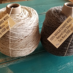 May include: Two skeins of Navajo Churro wool yarn. One skein is natural white and the other is natural light silver. Both skeins are labeled with the type of wool, color, and yardage. The white skein is 4 ply and has 450 yards. The silver skein is 2 ply and has 900 yards.