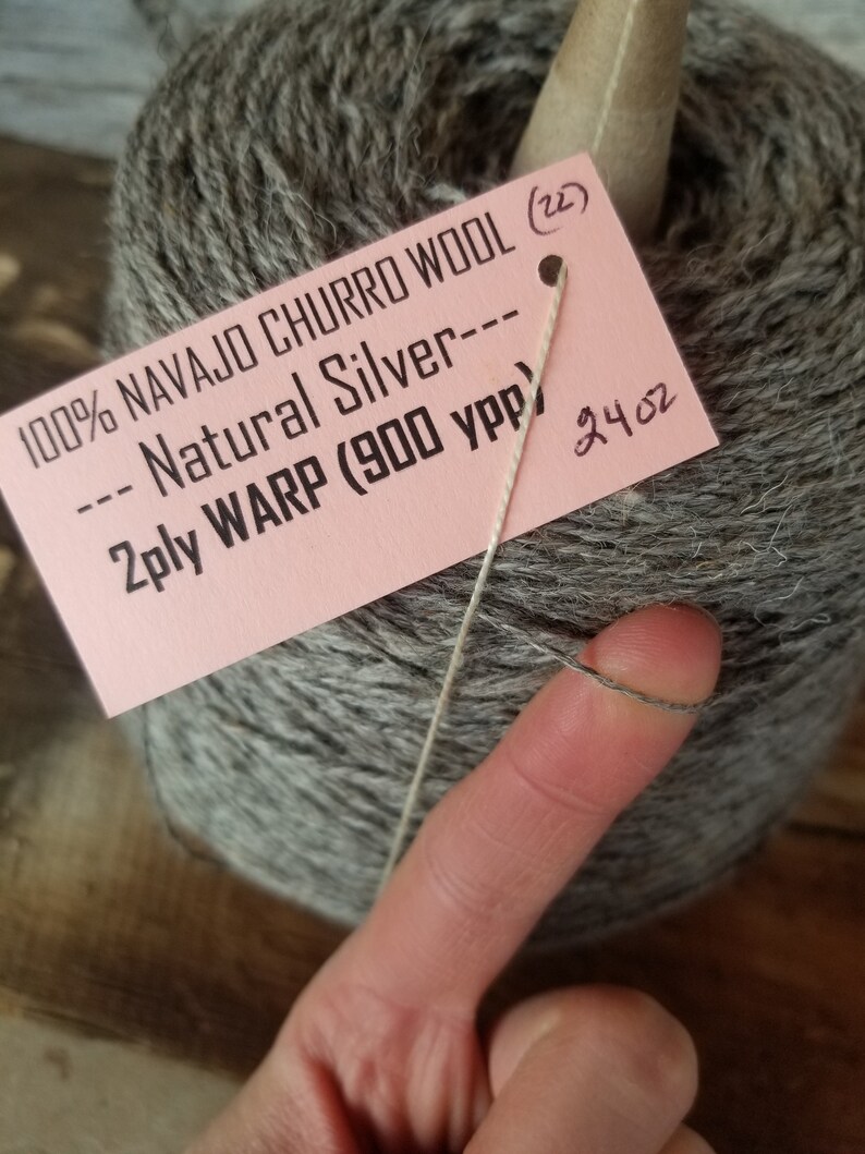 May include: A skein of 100% Navajo Churro wool yarn in a natural silver color. The label reads "100% Navajo Churro Wool (22) --- Natural Silver --- 2ply Warp (900 ypp) 24 oz".