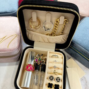 May include: Black velvet jewelry box with removable dividers. The box is open and contains a variety of jewelry, including rings, earrings, a necklace, and a lipstick. The box also has a small compartment for perfume bottles.
