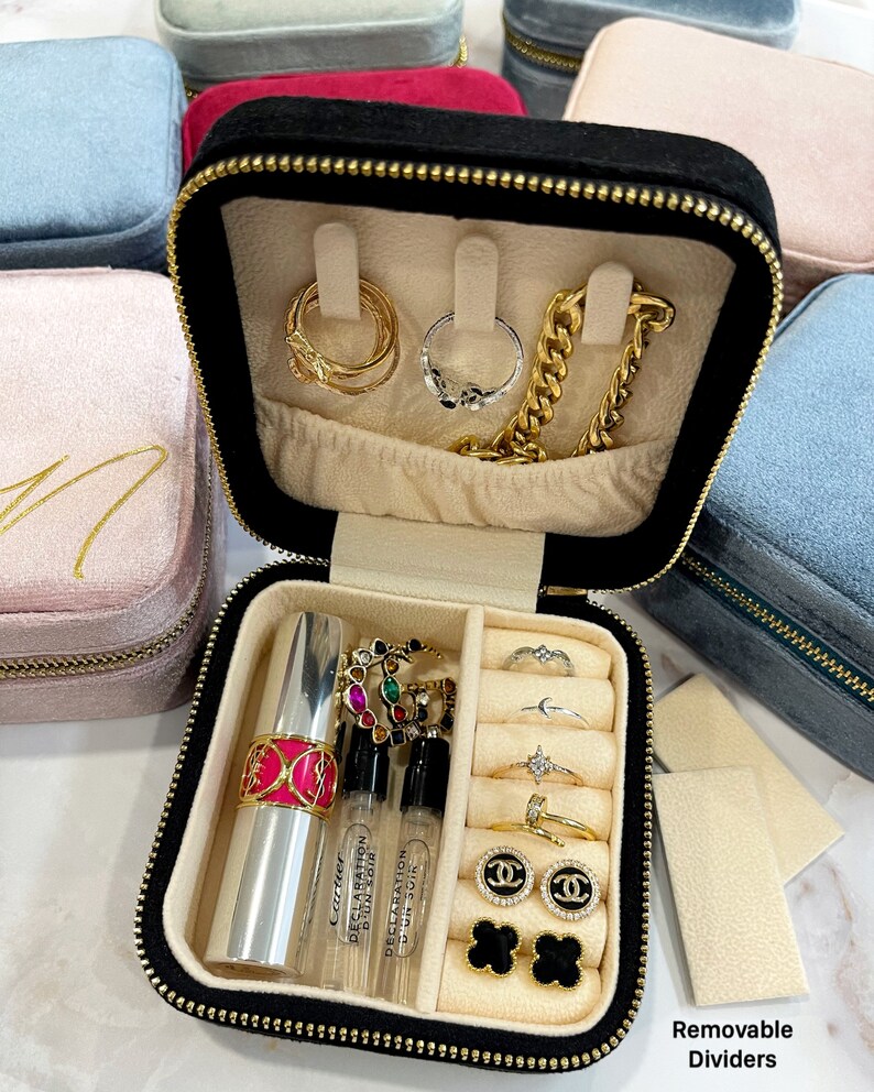 May include: Black velvet jewelry box with removable dividers. The box is open and contains a variety of jewelry, including rings, earrings, a necklace, and a lipstick. The box also has a small compartment for perfume bottles.