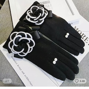 Op de afbeelding: Zwarte fleece handschoenen met een witte en zwarte bloemenversiering en witte parelknopen. De handschoenen liggen op een wit oppervlak met de tekst "minimalist design and architecture" en "2/7".