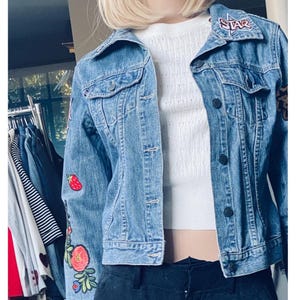 May include: A blue denim jacket with embroidered patches, including a strawberry, flowers, and a star with the word "STAR" on it.