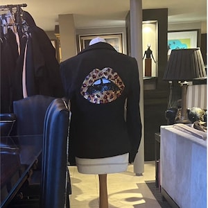 Puede incluir: Blazer negro con un diseño de labios de lentejuelas en rojo, dorado y negro.