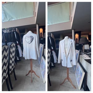 May include: Two white blazers on mannequins. The blazer on the left has a zebra print heart on the back. The blazer on the right has black star embellishments on the front.