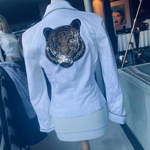 May include: White long-sleeved button-up shirt with a sequined tiger design on the back.