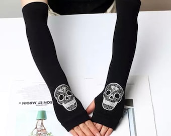 May include: A pair of black fingerless gloves with a silver skull design. The gloves are shown on a white surface. The text "Skull Gray" is visible below the gloves.