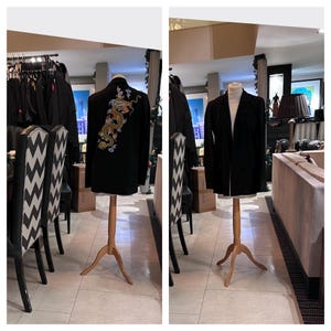 Puede incluir: Dos blazers negros exhibidos en maniquíes de madera. Un blazer presenta un bordado de dragón dorado en la espalda. El otro es un blazer negro liso clásico. Los blazers están en una habitación con sillas y un sofá.