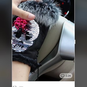 Può includere: Guanti invernali neri e bianchi con un design a forma di teschio in paillettes argentate e un bordo in pelliccia bianca. I guanti sono mostrati sul volante di un'auto.