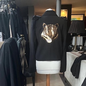 May include: A black blazer with gold sequined tiger detail on the back. The blazer has a cropped length and long sleeves.