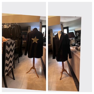 May include: Black blazer with gold star detail on the back, displayed on a wooden mannequin. The blazer has gold star accents on the shoulders. The background shows a room with furniture and clothing racks.
