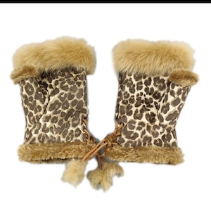 以下が含まれることがあります： ヒョウ柄とフェイクファーのトリムが付いたフィンガーレスグローブのペア。グローブは茶色の紐で結ばれており、両端に茶色のファーのポンポンが付いています。グローブはカーキ、赤、オレンジ、白、グレーからお選びいただけます。