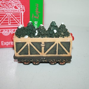 May include: A miniature wooden train car filled with small green Christmas trees, with the words "Alpine Tree Express" on the side of the car.
